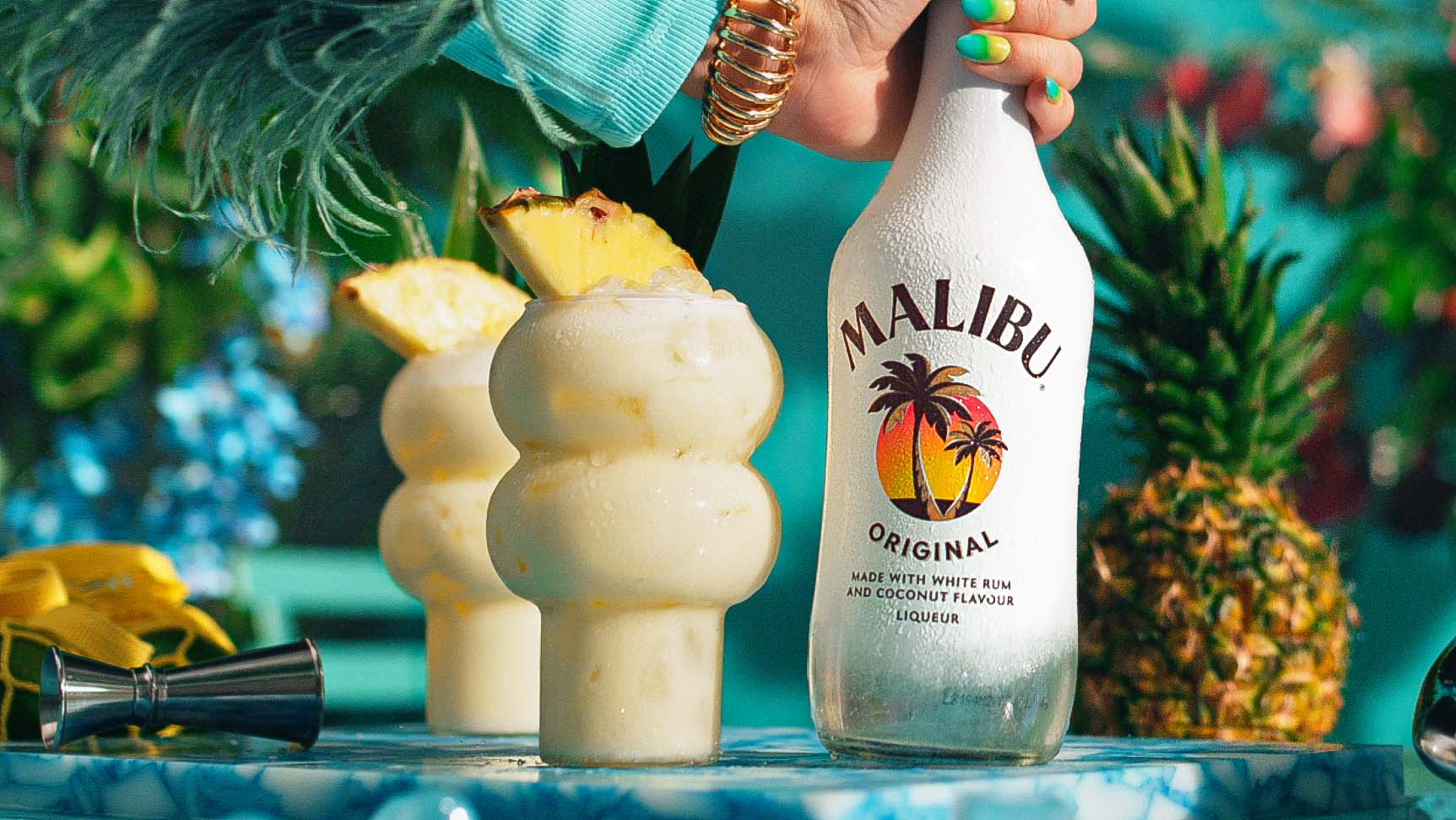 Two Malibu Pina Colada cocktails with a bottle of Malibu rum in a tropical setting