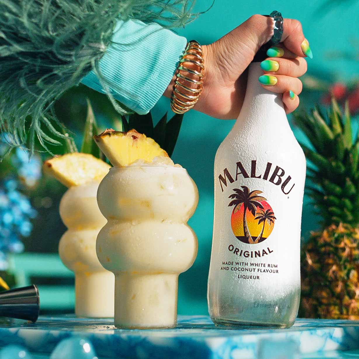 Two Malibu Pina Colada cocktails with a bottle of Malibu rum in a tropical setting