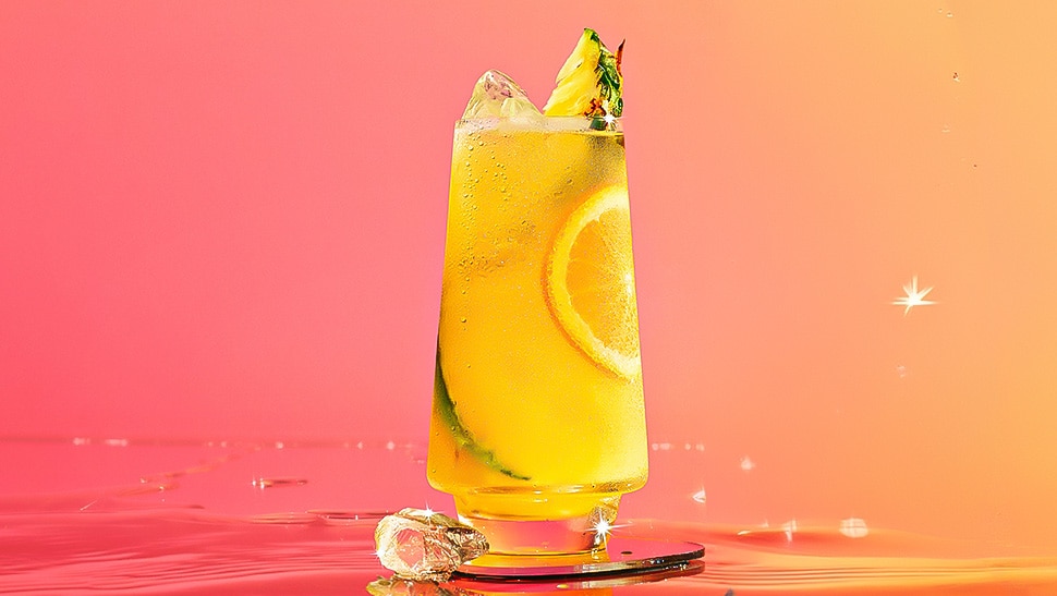 Malibu and pineapple juice cocktail on a glass coaster set in a pink/ yellow background